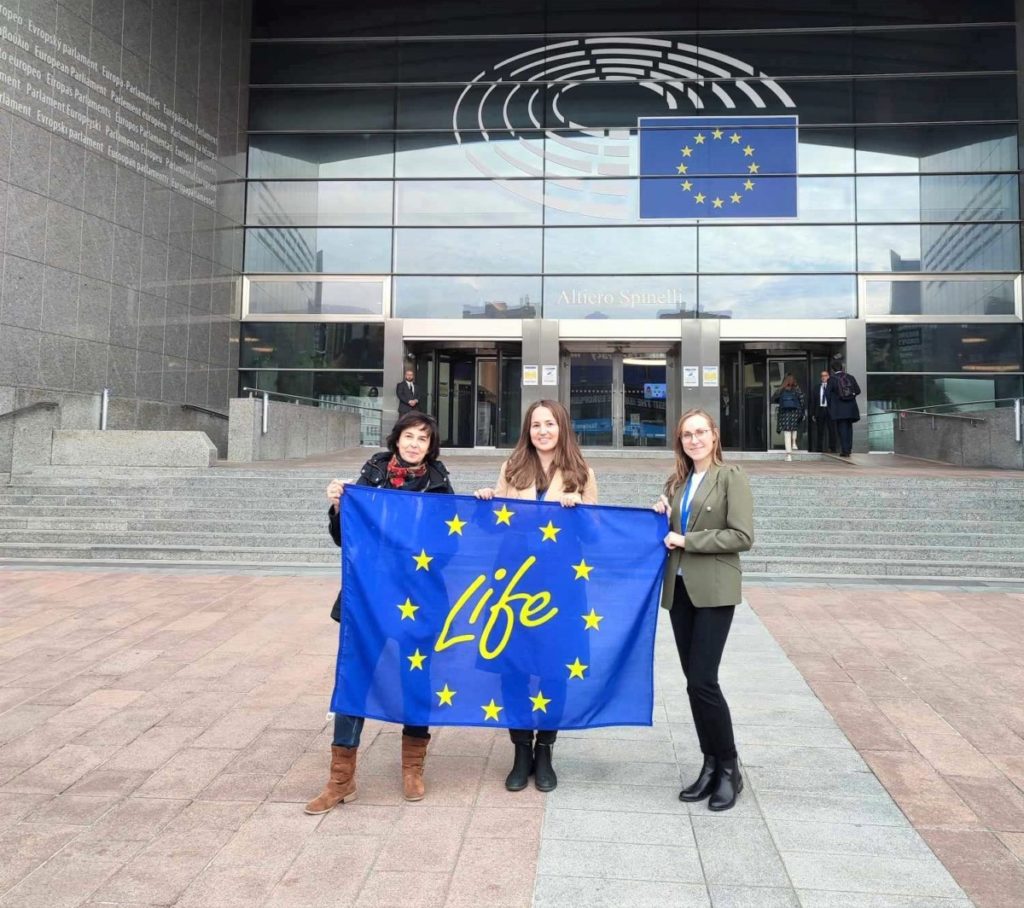 Przedstawicielki LIFE z flagą LIFE przed budynkiem Parlamentu Europejskieggo