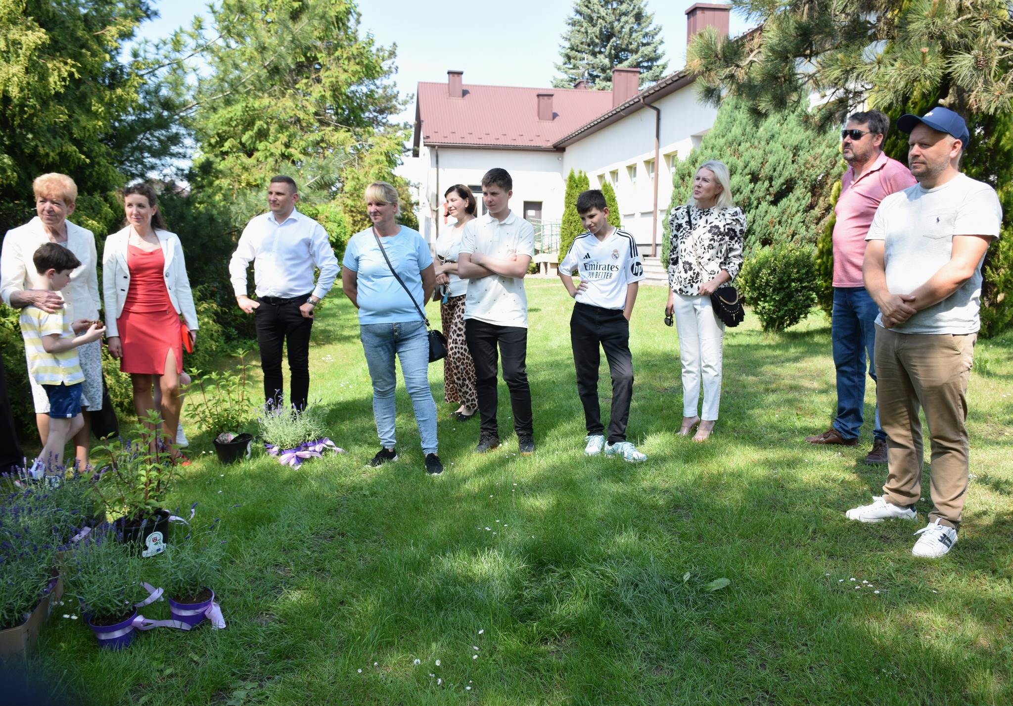 Grupa ludzi stoi na trawie przy roślinach miododajnych