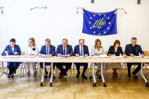 Osoby podpisują dokumenty pod flagą LIFE