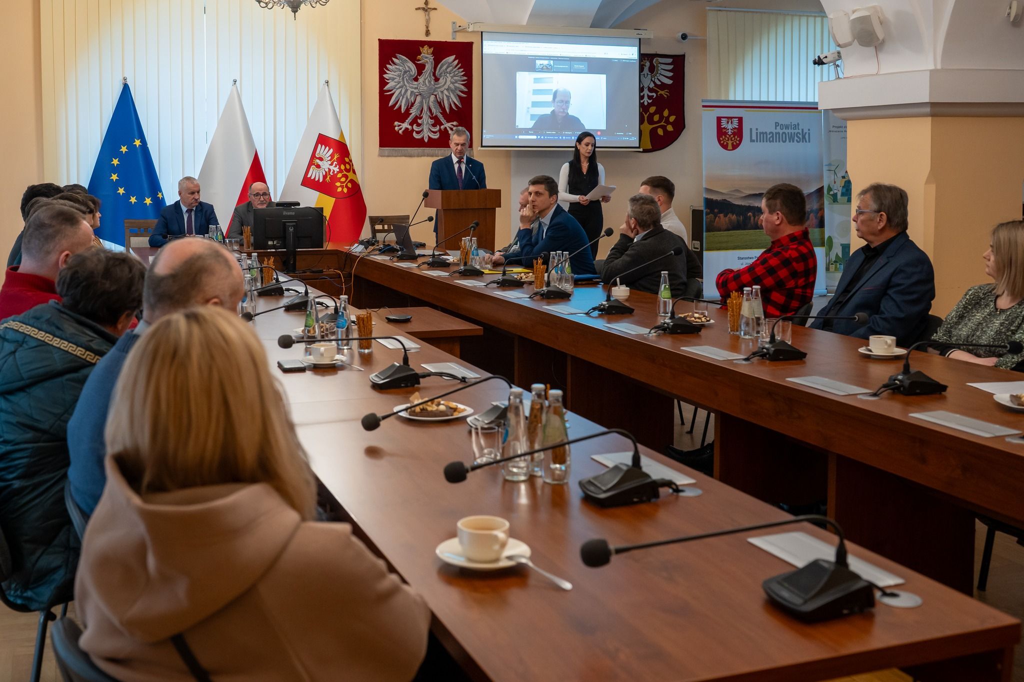 grupa ludzi siedzi przy stole w czasie konferencji i słucha przemówienia
