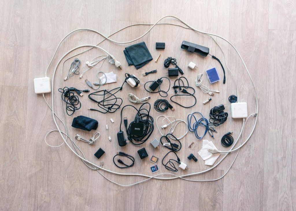 Zdjęcie przedstawi różne zasilacze, przejściówki, baterie i karty pamięci ułożone na drewnianej podłodze