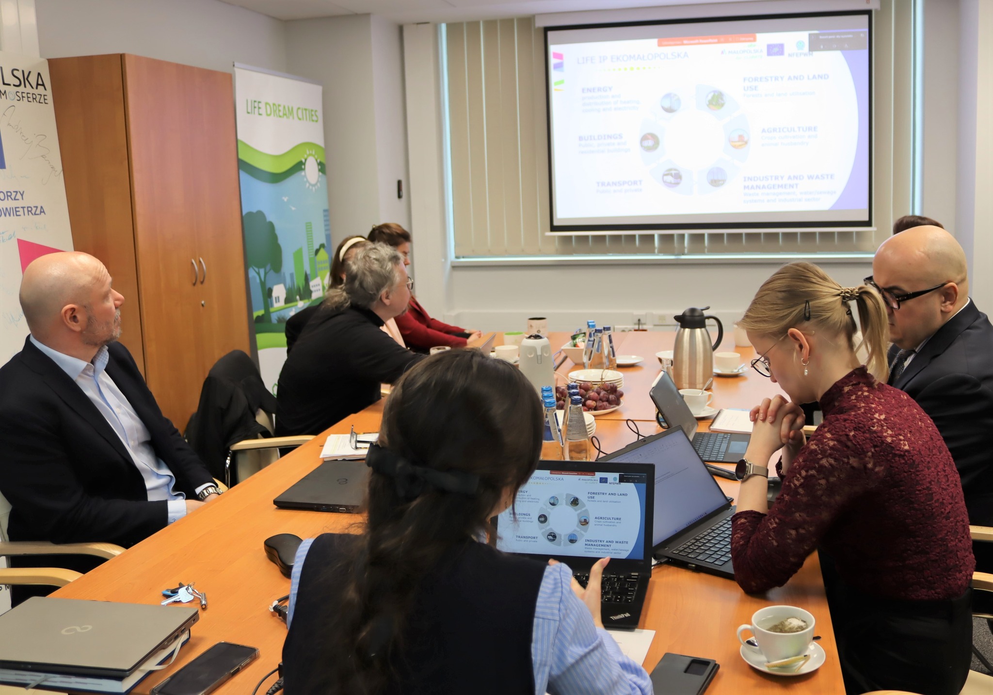 Kierownik projektu razem z monitorami i przedstawicielami doradców ds. klimatu i środowiska siedzi przy stole 