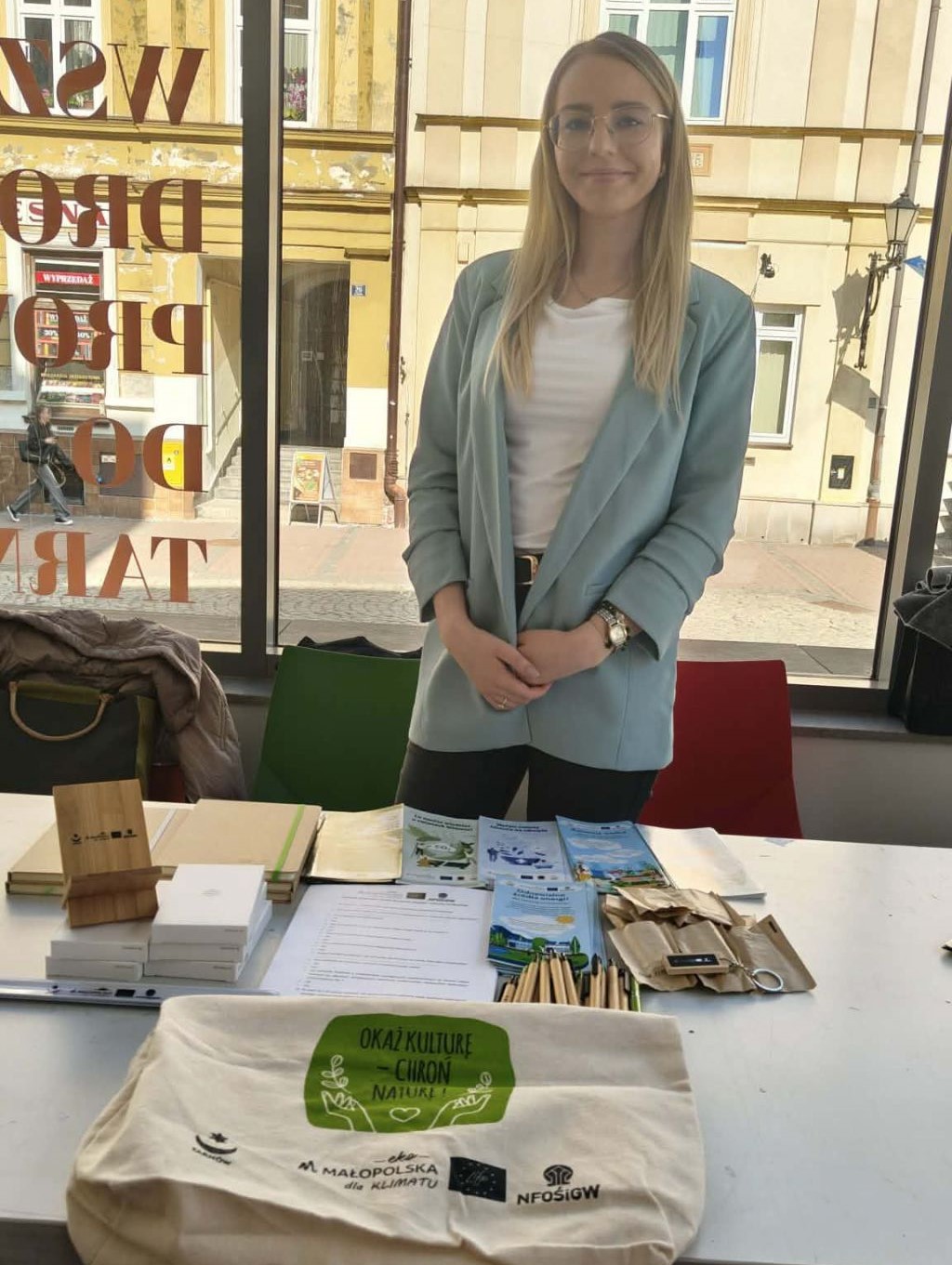 Kobieta zatrudniona na stanowisku doradcy ds. klimatu i środowiska stoi przy stoisku z gadgetami projektu LIFE EKOMAŁOPOLSKA