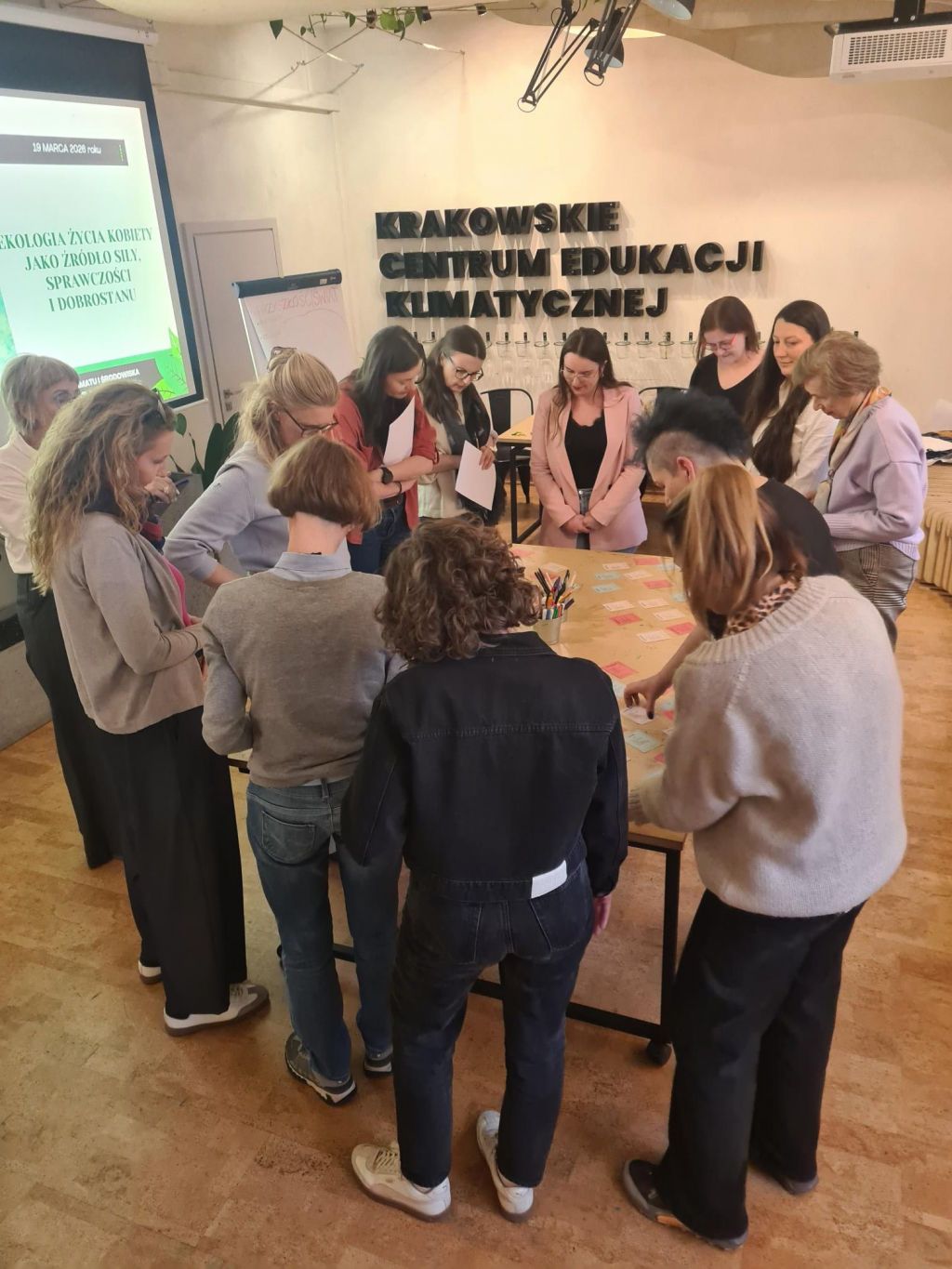 Grupa kobiet stoi przy stole z kolorowymi karteczkami, uczestniczą w warsztatach nt. emocji klimatycznych dla kobiet